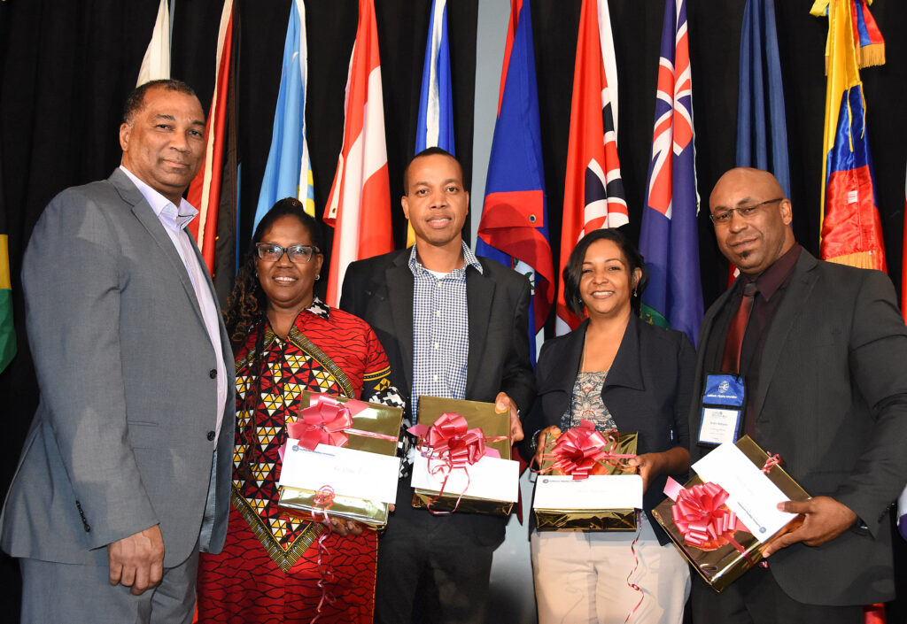 Five conference participants pose with wrapped gifts in front of national flags.