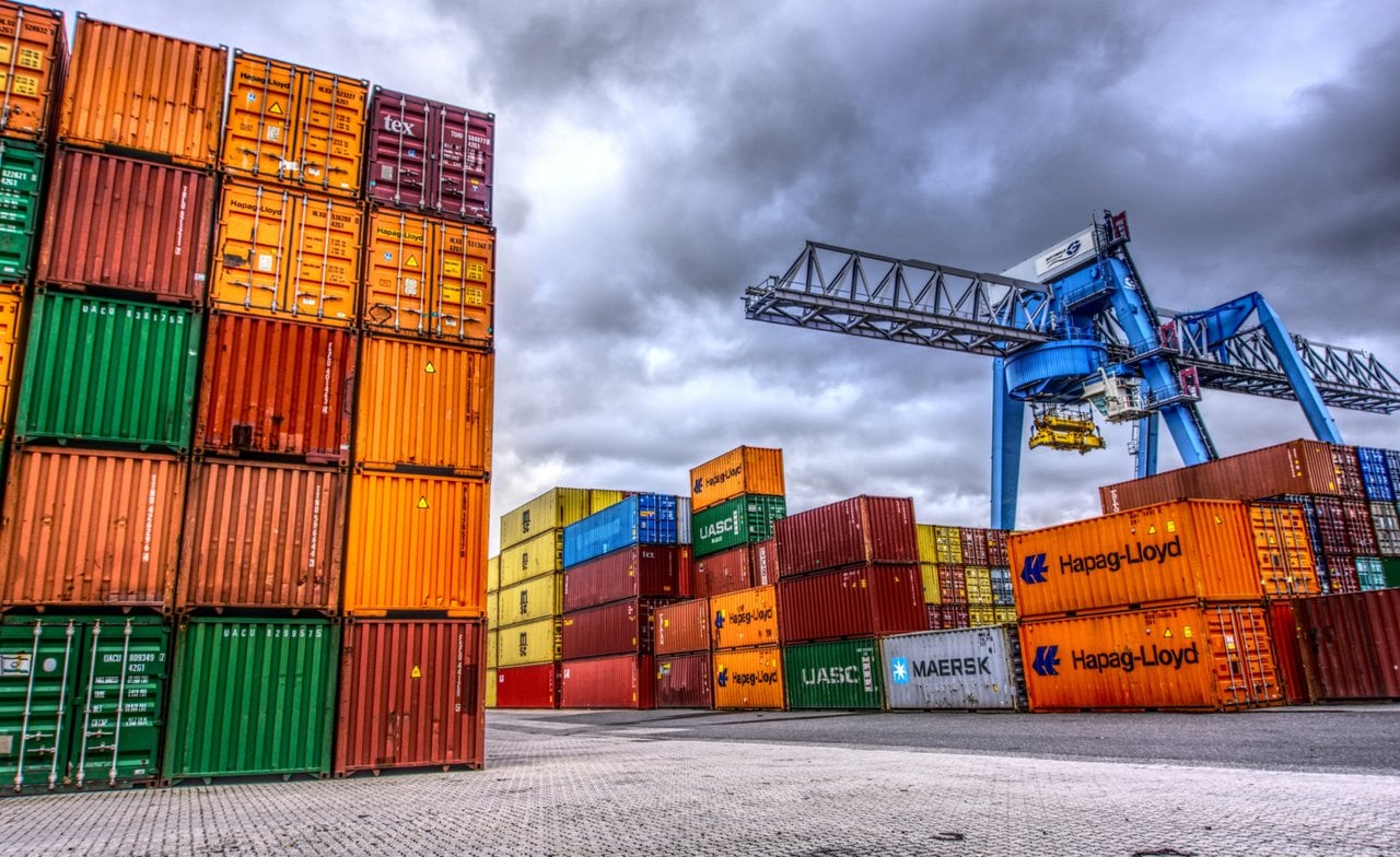 Stacked shipping containers beside a blue gantry crane at a port.